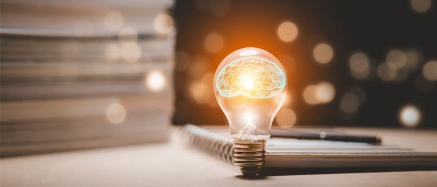 Image of a light bulb in front of a stack of notebooks